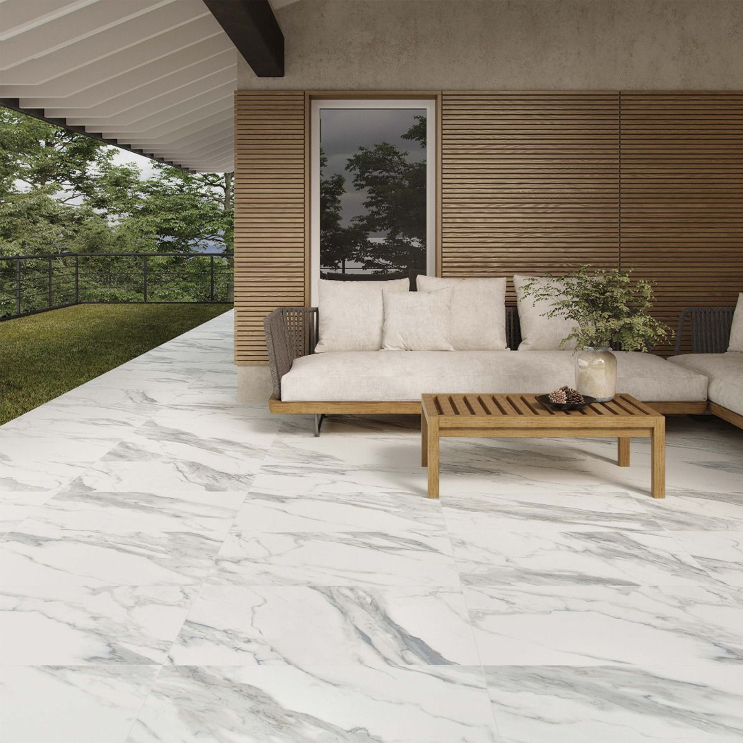 Outdoor porcelain tiles with marble-effect floor tiles with blue veining. There is a wooden corner sofa to the right.